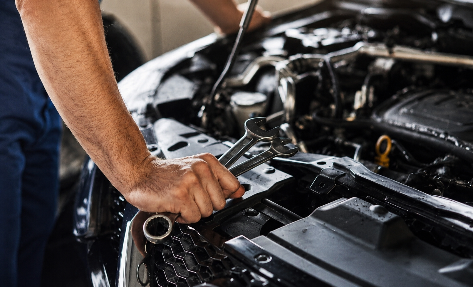 Technician holding wrenches while inspecting vehicle engine